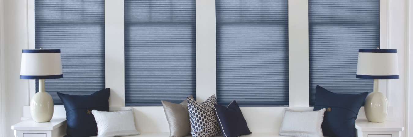 Blue cellular shades on four windows in a white wall over a window seat
